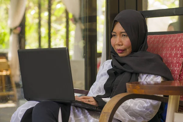 Estilo de vida retrato de meia idade asiático indonésio muçulmano mulher no tradicional hijab cabeça cachecol trabalhando relaxado em casa executando negócios on-line no sucesso do trabalho na internet — Fotografia de Stock