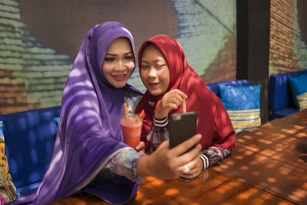 Mulher muçulmana e sua filha adolescente. Menina indonésia asiática feliz tomando selfie com sua bela mãe tanto no tradicional lenço cabeça hijab islâmico juntos no café — Fotografia de Stock