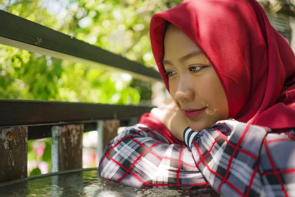 Lifestyle πορτρέτο των νέων όμορφη και χαλαρή Ασίας ινδονησιακή μουσουλμανική κορίτσι κάθεται σε εξωτερικούς χώρους φορώντας παραδοσιακή ισλαμική μαντίλα κεφάλι κασκόλ σκέψης και ονειροπόληση χαρούμενος — Φωτογραφία Αρχείου