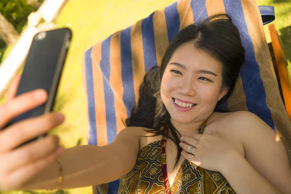 Joven hermosa y feliz turista asiática coreana mujer tomando selfie en tropical resort piscina hamaca sonriente despreocupado y natural en vacaciones de verano escapada — Foto de Stock