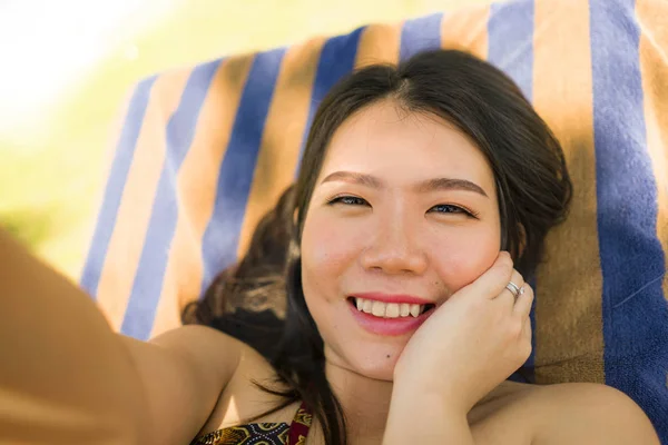 若い美しく、幸せな観光客アジアの女性は、夏休みの休暇で気楽で自然な笑顔のトロピカルリゾートプールハンモックで自分撮りを取ります — ストック写真