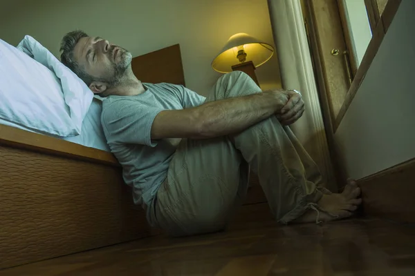 Νέος καταθλιπτικός και απελπισμένος άνθρωπος κάθεται στο υπνοδωμάτιο πάτωμα δίπλα στο κρεβάτι υποφέρουν κατάθλιψη και άγχος νιώθοντας συγκλονισμένοι και αβοήθητοι — Φωτογραφία Αρχείου