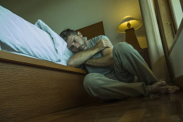Junger depressiver und verzweifelter Mann sitzt auf dem Schlafzimmerboden neben dem Bett und leidet unter Depressionen und Angstzuständen, die sich überfordert und hilflos fühlen — Stockfoto