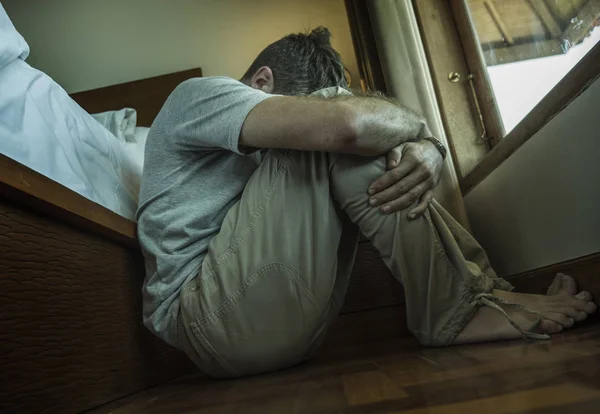 Ung deprimerad och desperat man sitter på sovrummet golvet bredvid sängen lidande depression och ångestkänsla överväldigad och hjälplös — Stockfoto