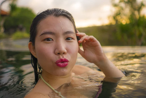 Молодая красивая и счастливая азиатская китаянка в бикини наслаждается закатом, делая селфи на удивительном курорте джунглей бесконечный бассейн, расслабляясь в летние каникулы — стоковое фото