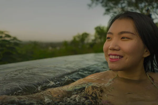 Tropical holidays lifestyle portrait of young beautiful and happy Asian Korean woman in bikini enjoying sunset at amazing jungle resort infinity pool swimming relaxed — Stock Photo, Image