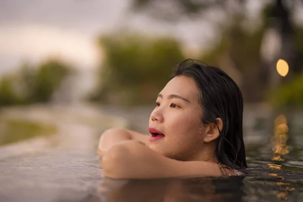 Tropical holidays lifestyle portrait of young beautiful and happy Asian Korean woman in bikini enjoying sunset at amazing jungle resort infinity pool swimming relaxed — Stock Photo, Image