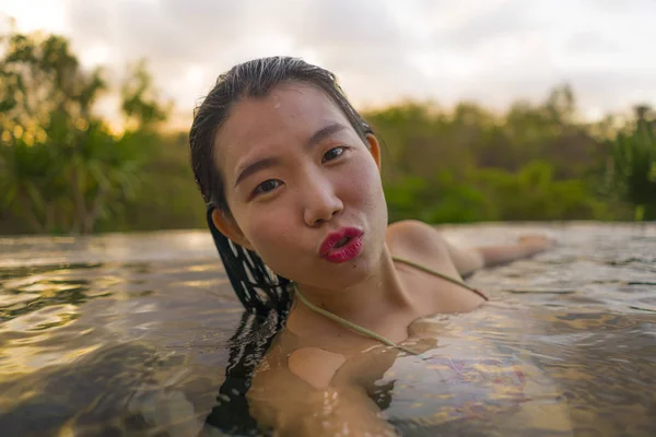 Joven hermosa y feliz mujer china asiática en bikini disfrutando de la puesta del sol tomando selfie en increíble selva resort piscina infinita natación relajado en vacaciones de verano — Foto de Stock