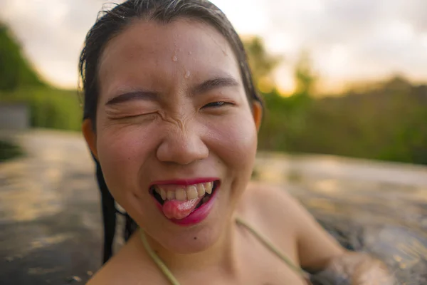 Молодая красивая и счастливая азиатская кореянка в бикини наслаждается закатом, делая селфи в удивительных джунглях курорта бесконечности бассейн расслабился в летние каникулы — стоковое фото