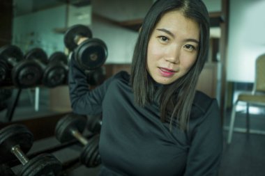 vücut bakımı ve sağlıklı yaşam tarzı kaldırma egzersiz sırasında halter raf tarafından oturan fitness merkezinde serin poz spor kapüşonlu genç güzel ve mutlu Asyalı Çinli kadın