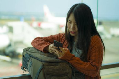 genç güzel ve mutlu Asyalı Koreli kadın tatil seyahat için hazır biniş bekliyor sırt çantası taşıyan havaalanı kalkış salonunda cep telefonu kontrol 