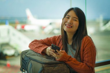 genç güzel ve mutlu Asyalı Çinli kadın tatil seyahat gülümseyerek hazır biniş bekliyor sırt çantası taşıyan havaalanı kalkış salonunda cep telefonu kontrol