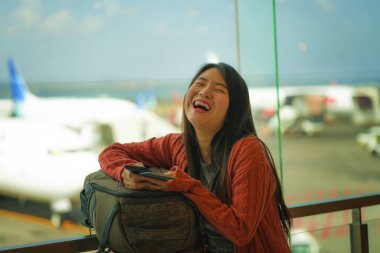 genç güzel ve mutlu Asyalı Çinli kadın biniş için bekleyen sırt çantası taşıyan havaalanı kalkış salonunda pasaport tutan cep telefonu kontrol