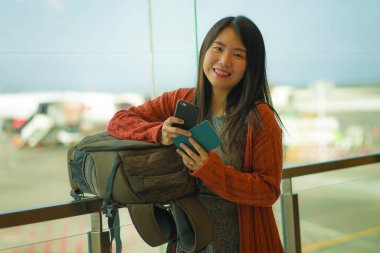 genç güzel ve mutlu Asyalı Japon kadın biniş için bekleyen sırt çantası taşıyan havaalanı kalkış salonunda pasaport tutan cep telefonu kontrol