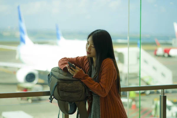 Young beautiful and happy Asian Korean woman checking mobile phone holding passport in her hand at airport departure lounge carrying backpack waiting for boarding — Stock Photo, Image