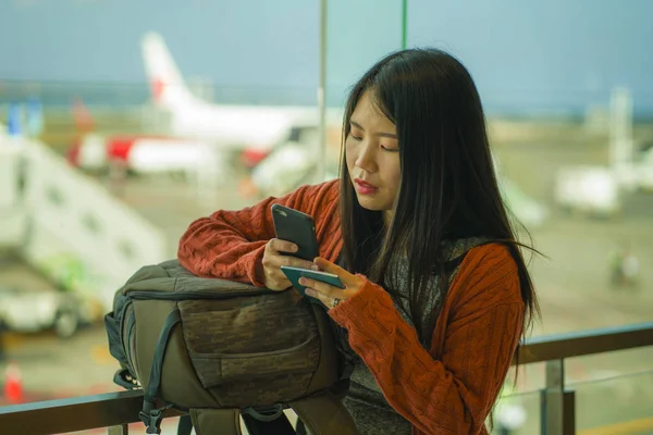 genç güzel ve mutlu Asyalı Koreli kadın biniş için bekleyen sırt çantası taşıyan havaalanı kalkış salonunda elinde pasaport tutan cep telefonu kontrol
