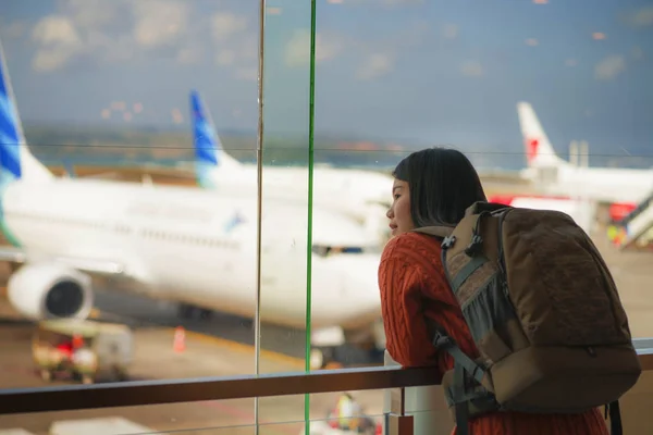 Young happy and excited Asian Chinese student woman with backpack at airport departure lounge watching aircraft through glass window smiling ready for boarding — Stock Photo, Image