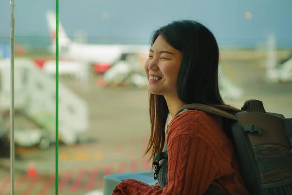 Young happy and excited Asian Korean student woman with backpack at airport departure lounge watching aircraft through glass window smiling ready for boarding — Stock Photo, Image