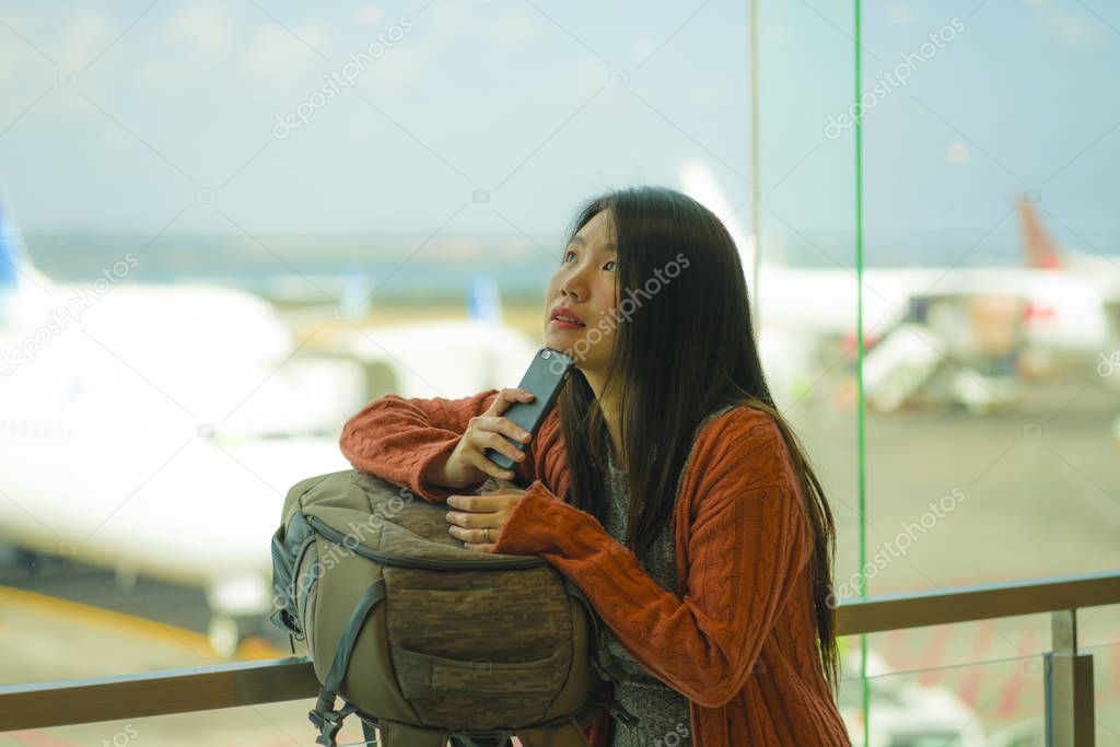 young beautiful and happy Asian Japanese woman checking mobile phone at airport departure lounge carrying backpack waiting for boarding thoughtful and pensive