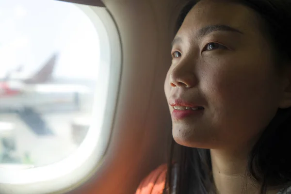 young happy and beautiful Asian Chinese tourist woman smiling excited sitting in airplane by the window arriving destination in aircraft transportation and holidays travel