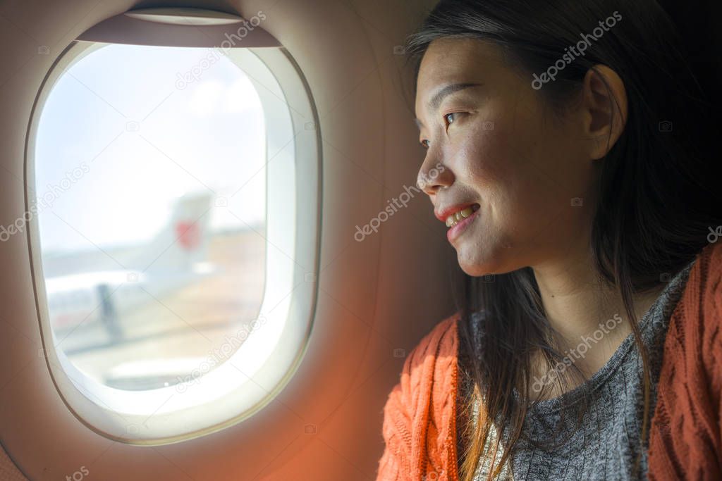 young happy and beautiful Asian Japanese tourist woman smiling excited sitting in airplane by the window arriving destination in aircraft transportation and holidays travel