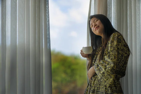 Стиль жизни портрет молодой красивой счастливой и расслабленной азиатской японской женщины в стильном халате у окна роскошного номера отеля с утренним кофе наслаждаясь тропическим видом — стоковое фото
