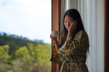 lüks otel odası penceresi ile şık bornoz genç güzel mutlu ve rahat Asyalı Çinli kadının yaşam tarzı portre tropikal görünümü zevk sabah kahvesi sahip