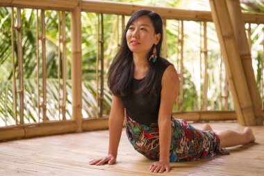 tropikal orman manzaralı güzel ahşap joglo stüdyoda yoga ve meditasyon egzersiz açık havada pratik genç doğal ve çekici Asyalı Çinli kadın