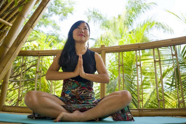 Young natural and attractive Asian Chinese woman practicing yoga and meditation exercise outdoors at beautiful wooden joglo studio with tropical jungle view — Stock Photo, Image