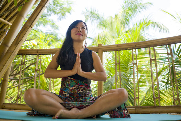 young natural and attractive Asian Chinese woman practicing yoga and meditation exercise outdoors at beautiful wooden joglo studio with tropical jungle view