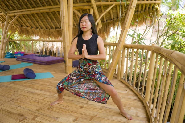 Jovem natural e atraente mulher chinesa asiática praticando ioga e exercício de meditação ao ar livre no belo estúdio de joglo de madeira com vista para a selva tropical — Fotografia de Stock