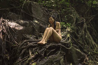 tropik büyülü ormanda güzel kadın . Genç çekici Asyalı Çinli kız bikini gizemli ve büyülü bir duygu ile tropikal cennet ormanda ağaç gövdesi üzerinde oturan