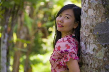 taze tropikal yağmur ormanlarında ağaç gövdesi üzerinde rüya gibi eğilerek doğanın güzelliği sakin zevk zarif yaz elbisesi genç güzel ve rahat Asyalı Çinli kadın 