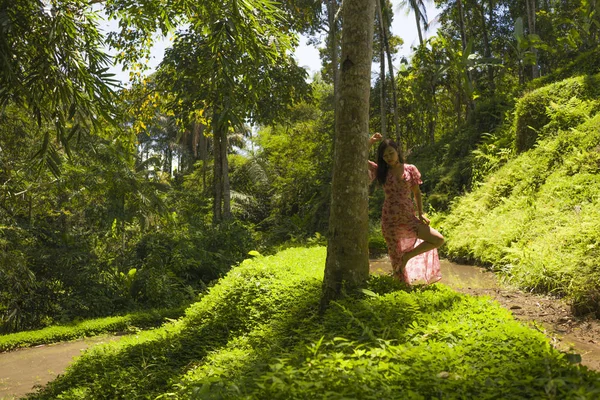 Mladá krásná a uvolněná Asijská Korejská žena v elegantních letních šatech s poklidnou krásou přírody, která se dotýká kmene stromů v čerstvém tropickém deštním lese — Stock fotografie