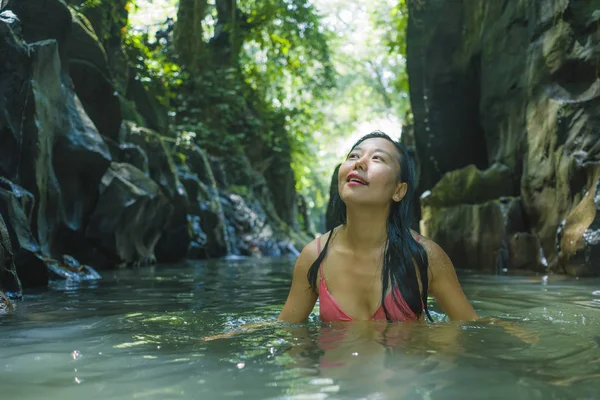 Счастливая азиатка в бикини, наслаждающаяся уникальным летним отдыхом в тропическом лесу, освежающая расслабленность в естественном бассейне, пораженная волшебным чувством на озере джунглей — стоковое фото