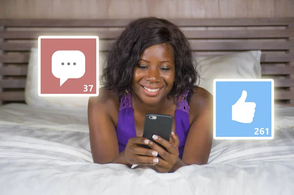happy black African American woman in pajamas using mobile phone social media smiling cheerful lying on bed at home receiving likes and comments in internet success