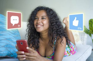 internet sosyal medya uygulaması seviyor ve sohbet yorum simgeleri genç güzel ve mutlu karışık etnik siyah Afro-Amerikan kadın evde cep telefonu kullanarak kompozit