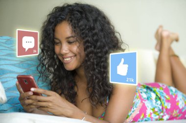 internet sosyal medya uygulaması seviyor ve sohbet yorum simgeleri cep telefonu kullanarak evde kanepede genç güzel ve mutlu karışık etnik İspanyol kadın kompozit