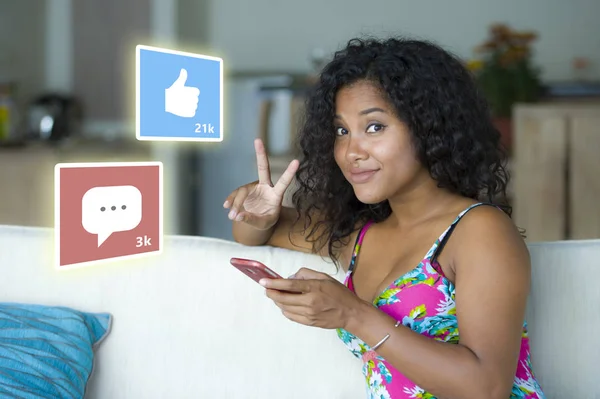 Internet social media app likes and chat comments icons composite on young beautiful and happy mixed ethnicity black African American woman at home couch using mobile phone — Stock Photo, Image