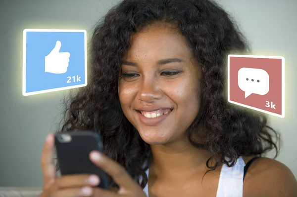 Internet social media app likes y chat comentarios iconos compuesto en joven hermosa y feliz mixta etnia negro afroamericana mujer en casa sofá usando teléfono móvil —  Fotos de Stock