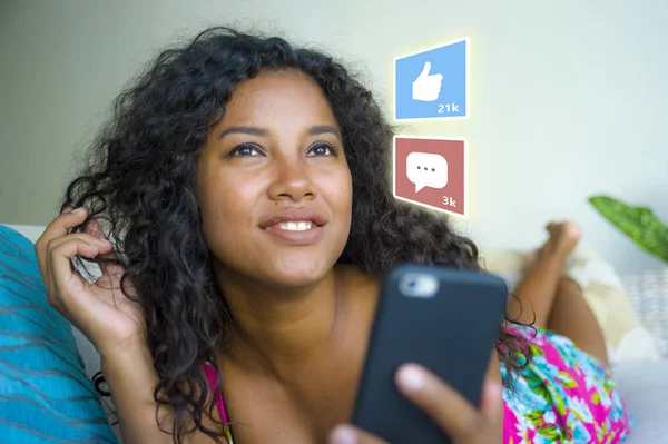 Internet social media app likes and chat comments icons composite on young beautiful and happy mixed ethnicity black African American woman at home couch using mobile phone — Stock Photo, Image