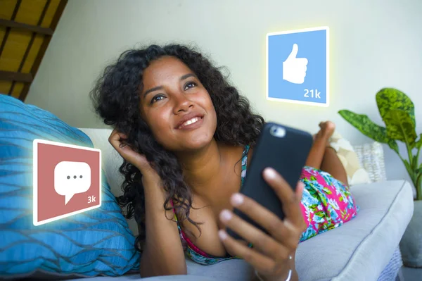 Internet social media app likes and chat comments icons composite on young beautiful and happy mixed ethnicity black African American woman at home couch using mobile phone — Stock Photo, Image