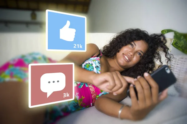 Internet social media app likes y chat comentarios iconos compuesto en joven hermosa y feliz mixta etnia hispana mujer en casa sofá usando teléfono móvil —  Fotos de Stock
