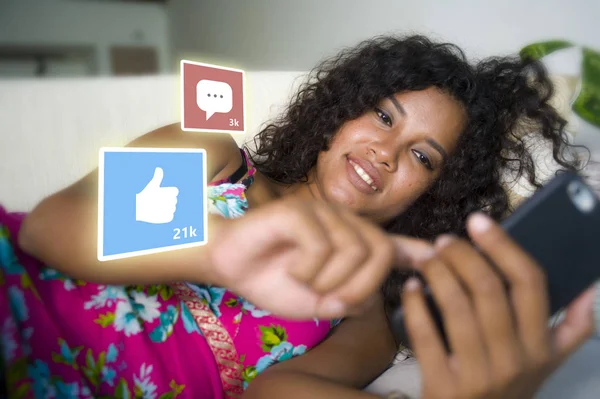 Internet social media app likes y chat comentarios iconos compuesto en joven hermosa y feliz mixta etnia latina afroamericana mujer en casa sofá usando teléfono móvil —  Fotos de Stock