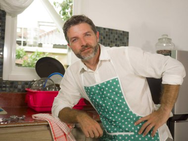 30'lardan 40'lı yıllara kadar mutlu ve çekici adam mutfak önlük giyen serin bulaşık yıkama zevk poz ve evde memnun gülümseyerek ev işleri yapıyor