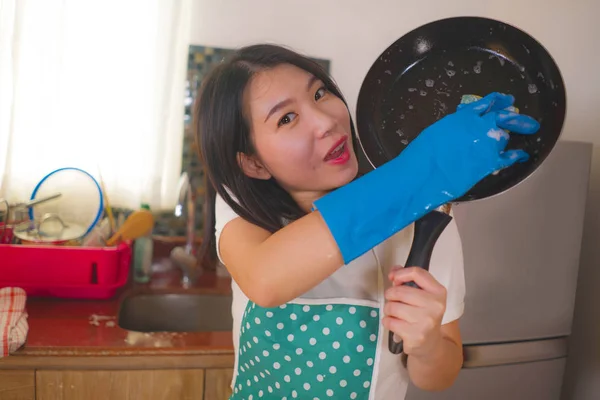 Natürliches Lifestyleporträt einer jungen schönen und glücklichen asiatischen Chinesin in Schürze und Handschuhspülen und Pfanne lächelnd in entspannter Hausarbeit und Hausarbeit — Stockfoto