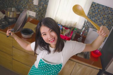 mutfak önlük tutan tava ve kaşık genç güzel ve mutlu Asyalı Koreli kadın neşeli ev işleri yemek ve housekeeping eğlenceli poz zevk gülümseyerek