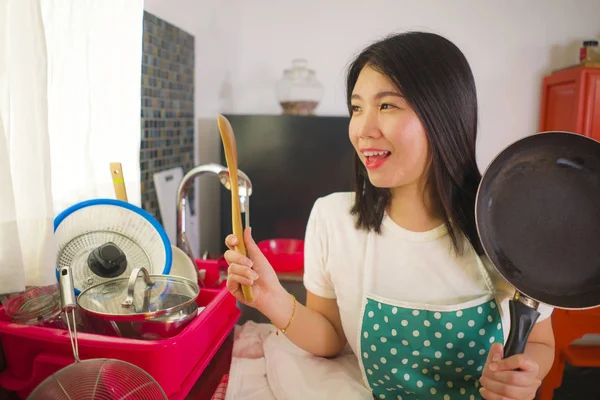 Jovem bela e feliz asiática chinesa mulher na cozinha avental segurando colher e cozinhar panela sorrindo alegre desfrutando de tarefas domésticas cozinheiro e limpeza — Fotografia de Stock