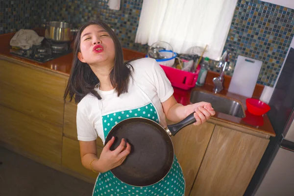 Young beautiful and happy Asian Korean woman in kitchen apron playing air guitar with cooking pan having fun enjoying domestic chores dancing and singing at home — Stock Photo, Image