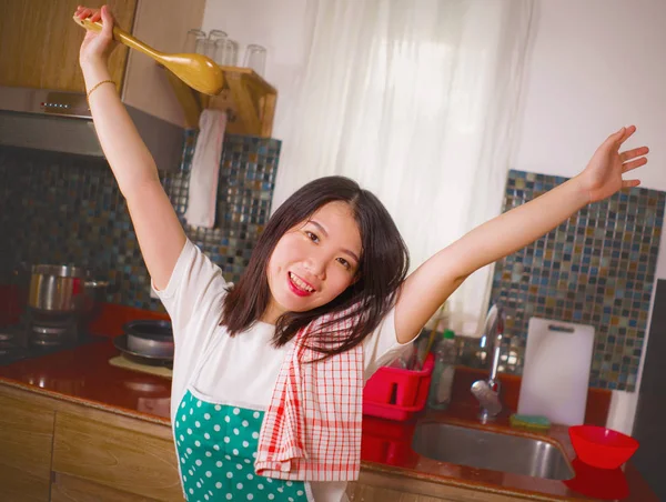 Retrato de estilo de vida natural de jovem bela e feliz mulher chinesa asiática no avental de cozinha segurando colher sorrindo alegre desfrutando de tarefas domésticas e limpeza — Fotografia de Stock